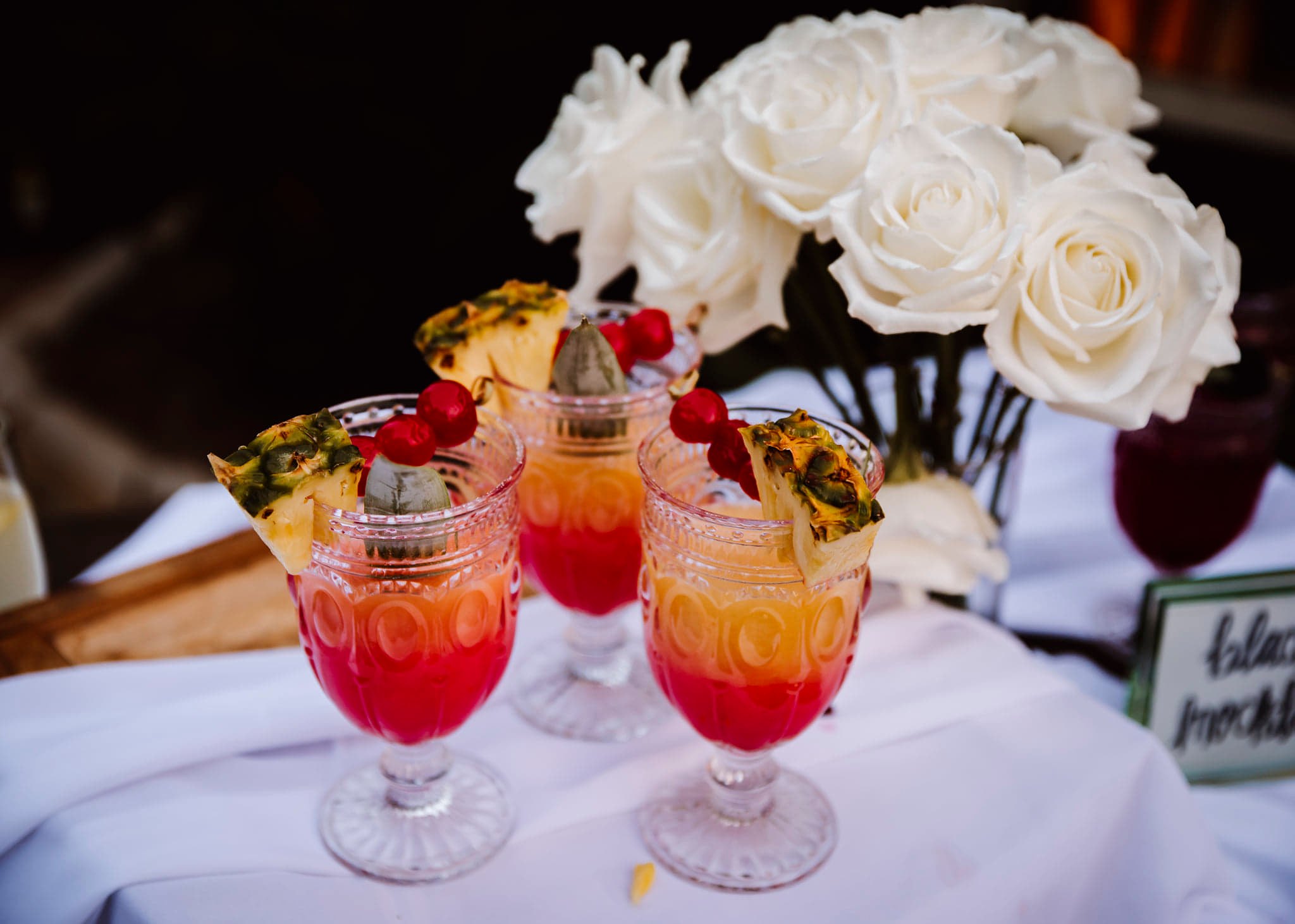 three fruit drink cocktails next to a white rose centerpiece