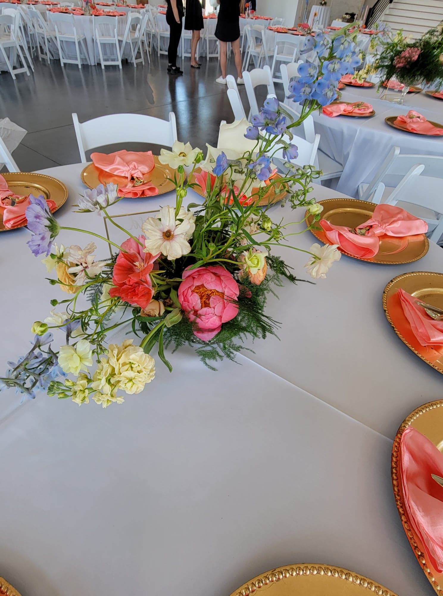 plated dinner set up for a wedding with a floral arrangement on white tablecloth with gold chargers and peach colored cloth napkins